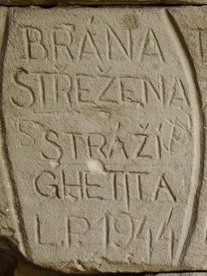 Inscription: Brána strežena stráží ghetta